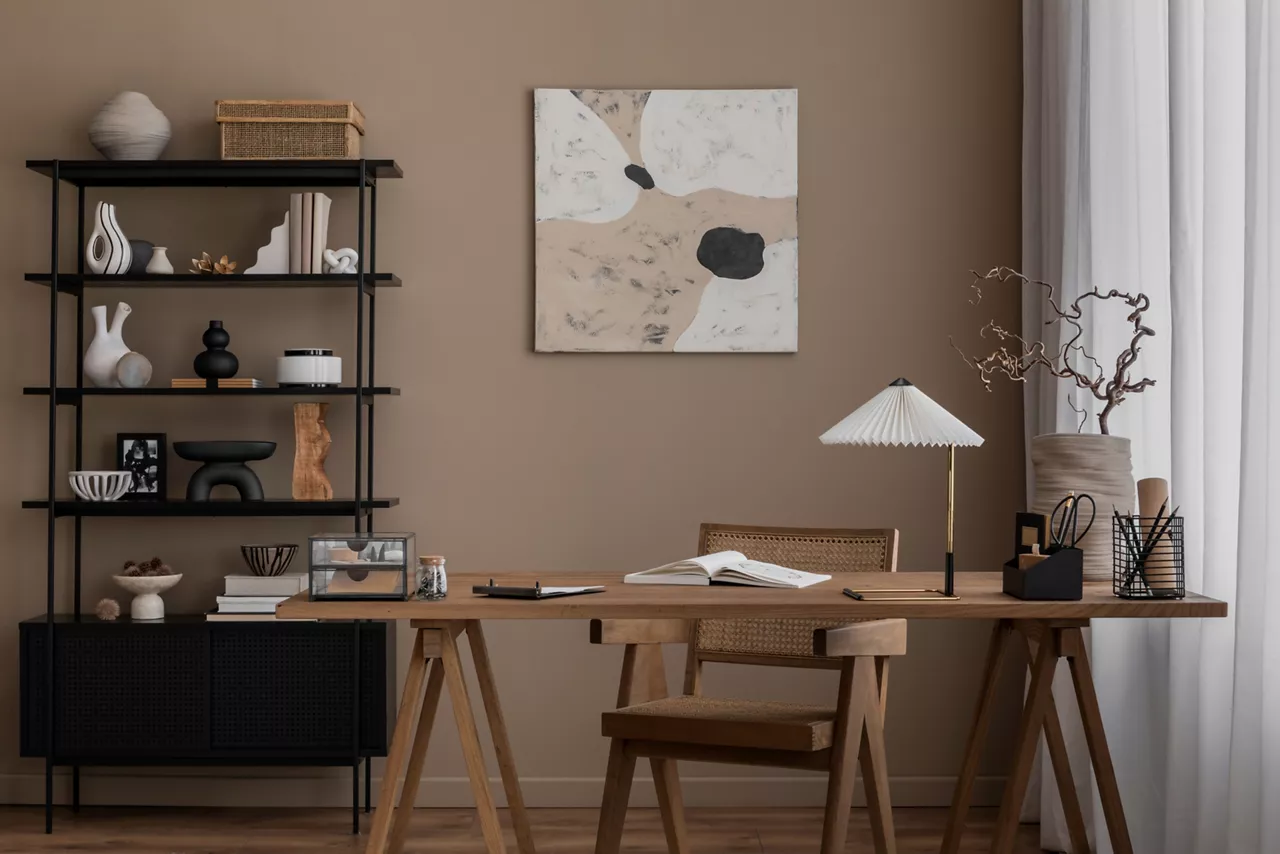 Aesthetic composition of living room interior with mock up poster frame, wooden desk, rattan chair, black rack, vase with branch, books, brown wall and office accessories. Home decor. Template.