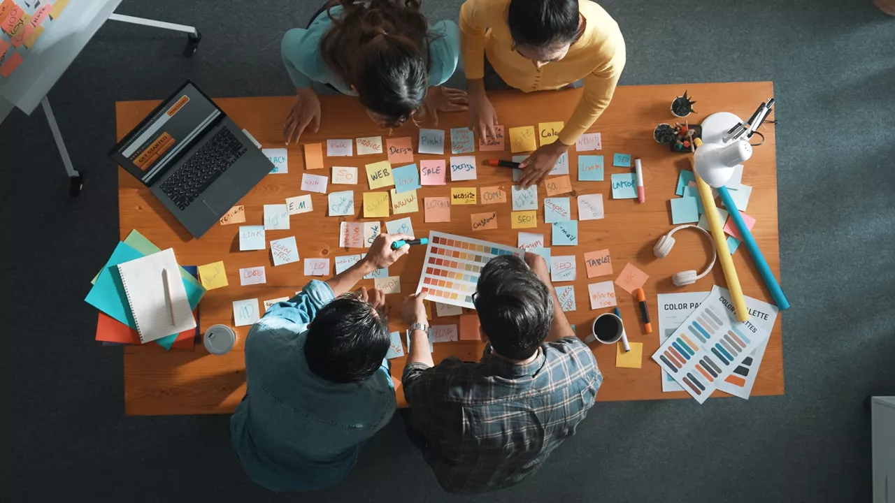 Time lapse of business team with casual outfit looking laptop screen and sharing idea. Aerial view of manager working and checking color palette at table with sticky notes and headphone. Symposium.