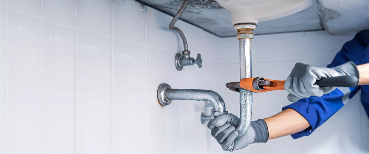 Technician plumber using a wrench to repair a water pipe under the sink. Concept of maintenance, fix water plumbing leaks, replace the kitchen sink drain, cleaning clogged pipes is dirty or rusty.