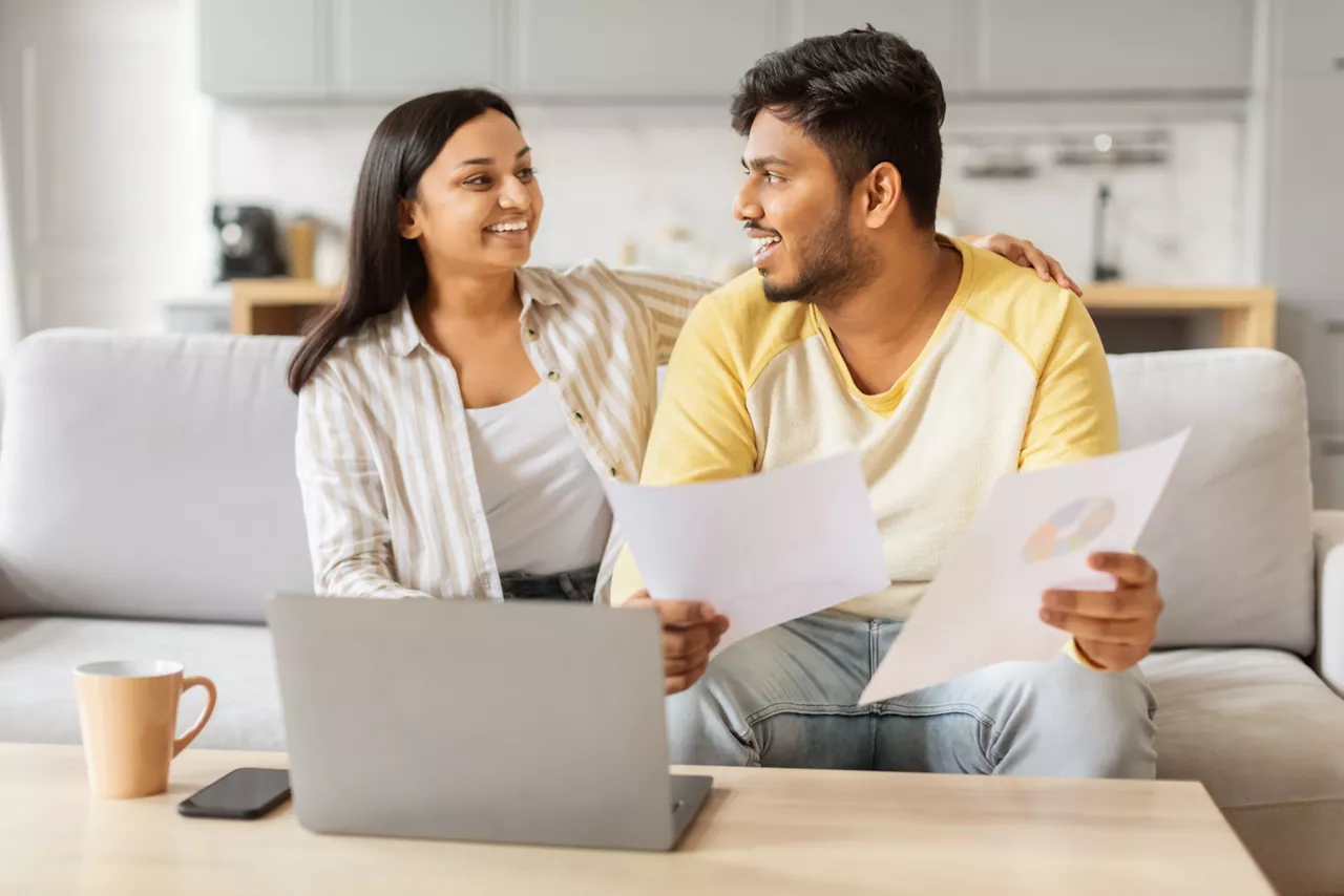 An eastern millennial couple casually engages in a discussion over paperwork with a laptop in the serene atmosphere of their home