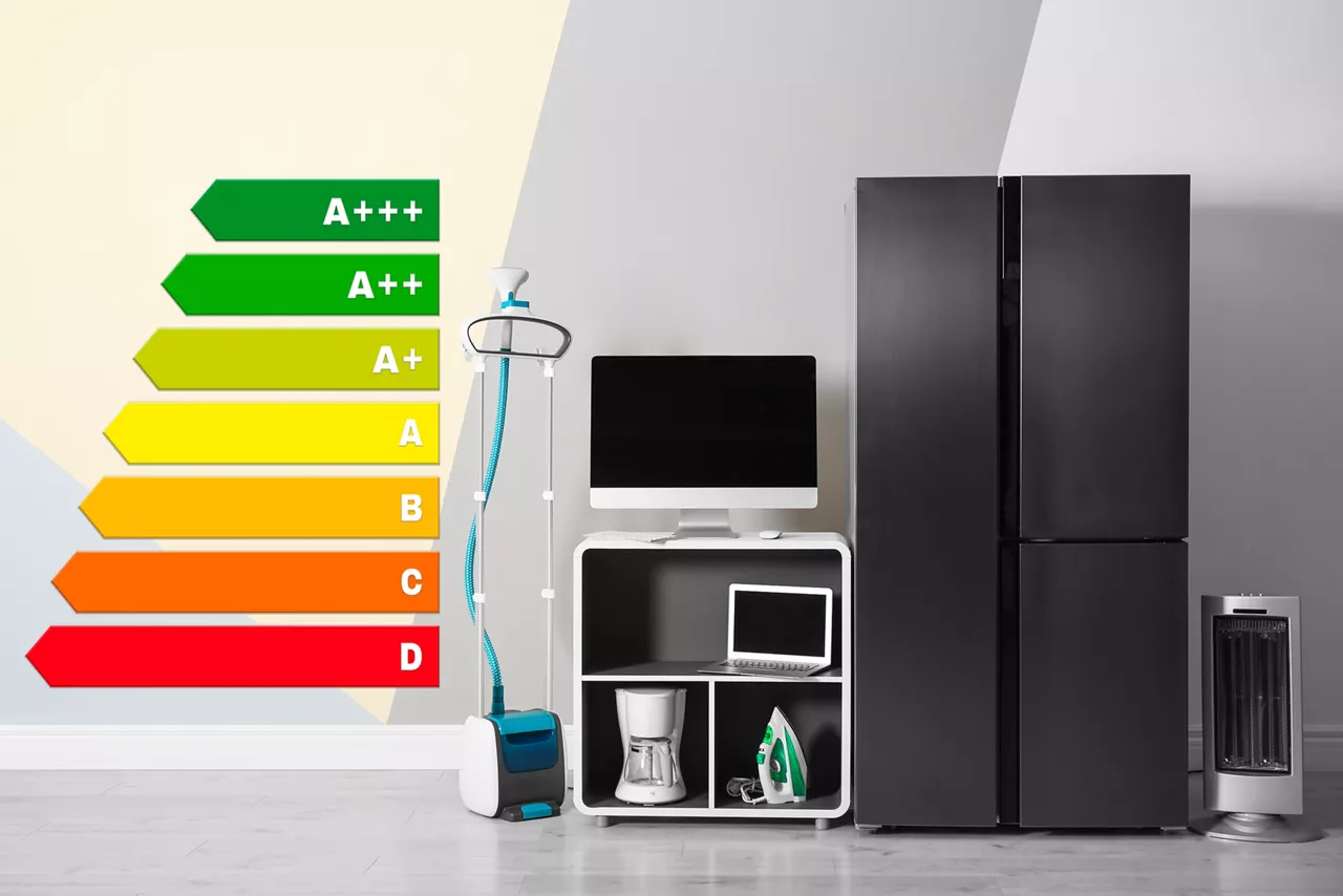 Energy efficiency rating label and different household appliances near color wall indoors