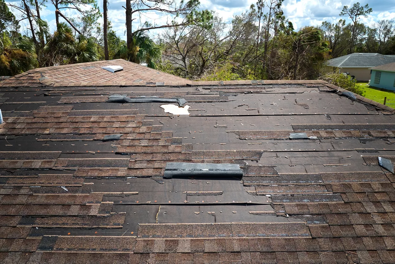Wind damaged house roof with missing asphalt shingles after hurricane Ian in Florida. Repair of home rooftop concept