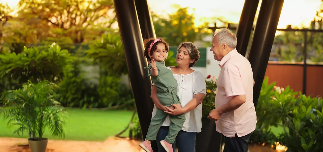 Happy Indian old grandmother standing holding cute little child girl in arms hands playing together outdoor home. Beautiful senior couple talking with small adorable daughter enjoying summer holiday