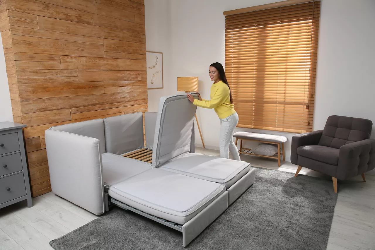 Young woman unfolding sofa into a bed in room. Modern interior