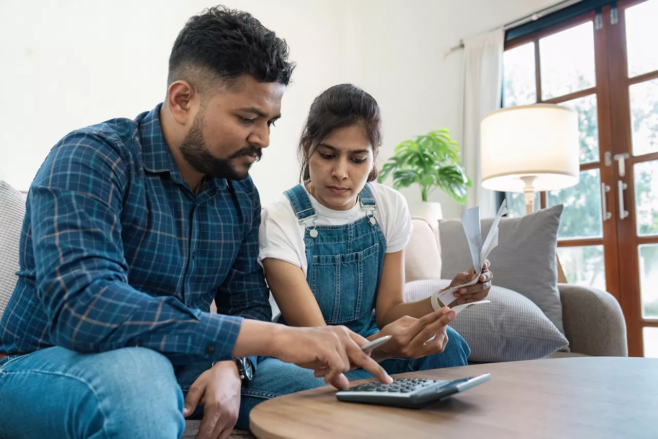 Indian couple managing household finances, paying bills, and planning budget together at home, showcasing teamwork and financial responsibility in a modern living room setting.