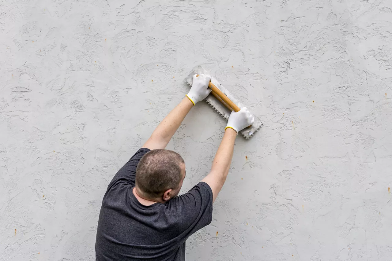 A dedicated craftsman applies texture to freshly plastered surface, showcasing craftsmanship under the warm morning light.