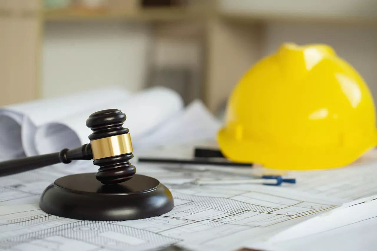 Labor and Construction law concept. judge gavel on building blueprint plans with a yellow safety helmet in the background. law that deals with matters relating to building construction, engineering. 