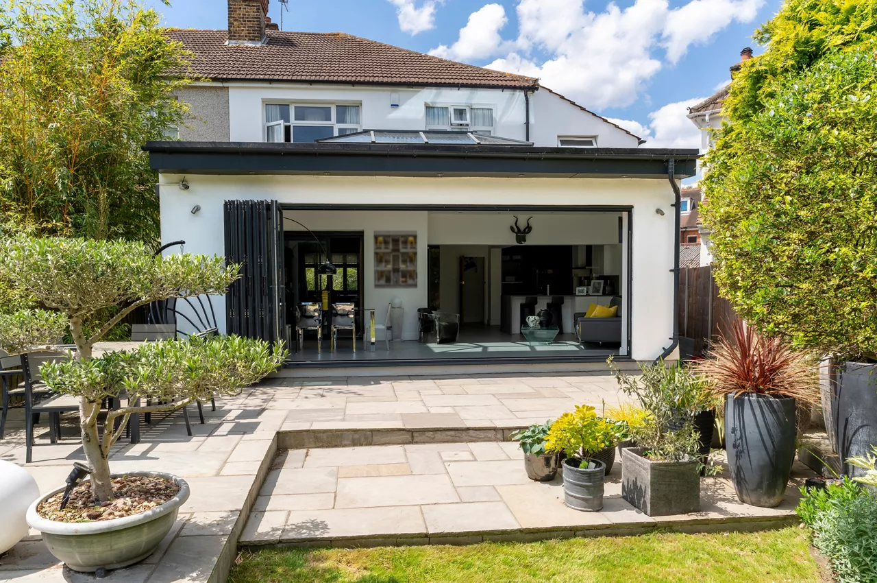 Stylish, open bifold doors with plants in summer, revealing interior of a designer, lifestyle, kitchen diner room. Indian sandstone patio.