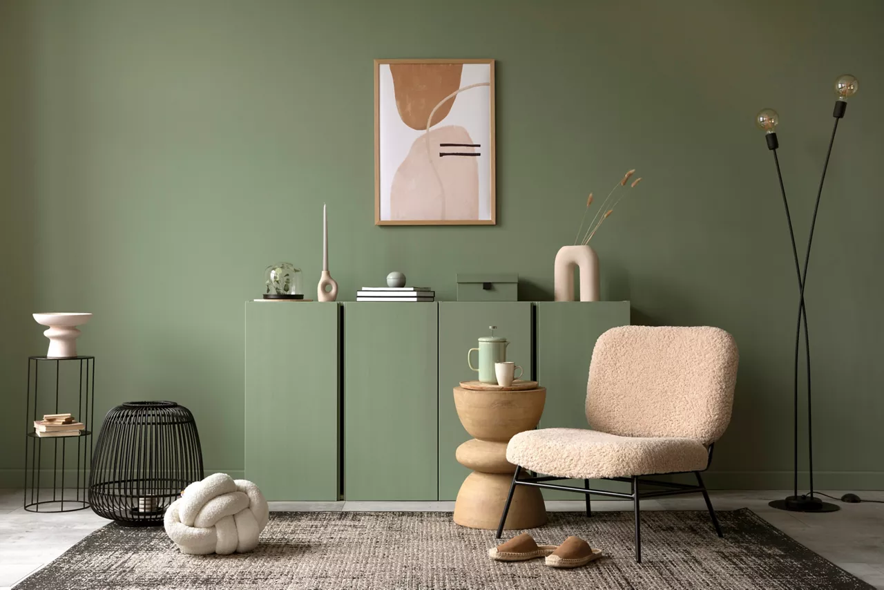 Stylish living room interior design with mock up poster frame, frotte armchair, wooden commode, side table, plants and creative home accessories. Sage green wall. Home staging. Template. Copy space.