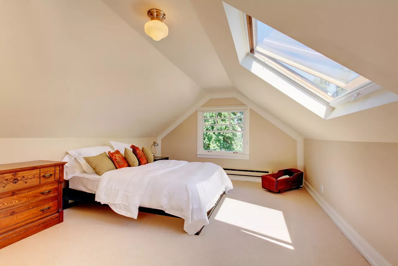 Attic modern bedroom with white bed and skylight and beige walls and carpet.