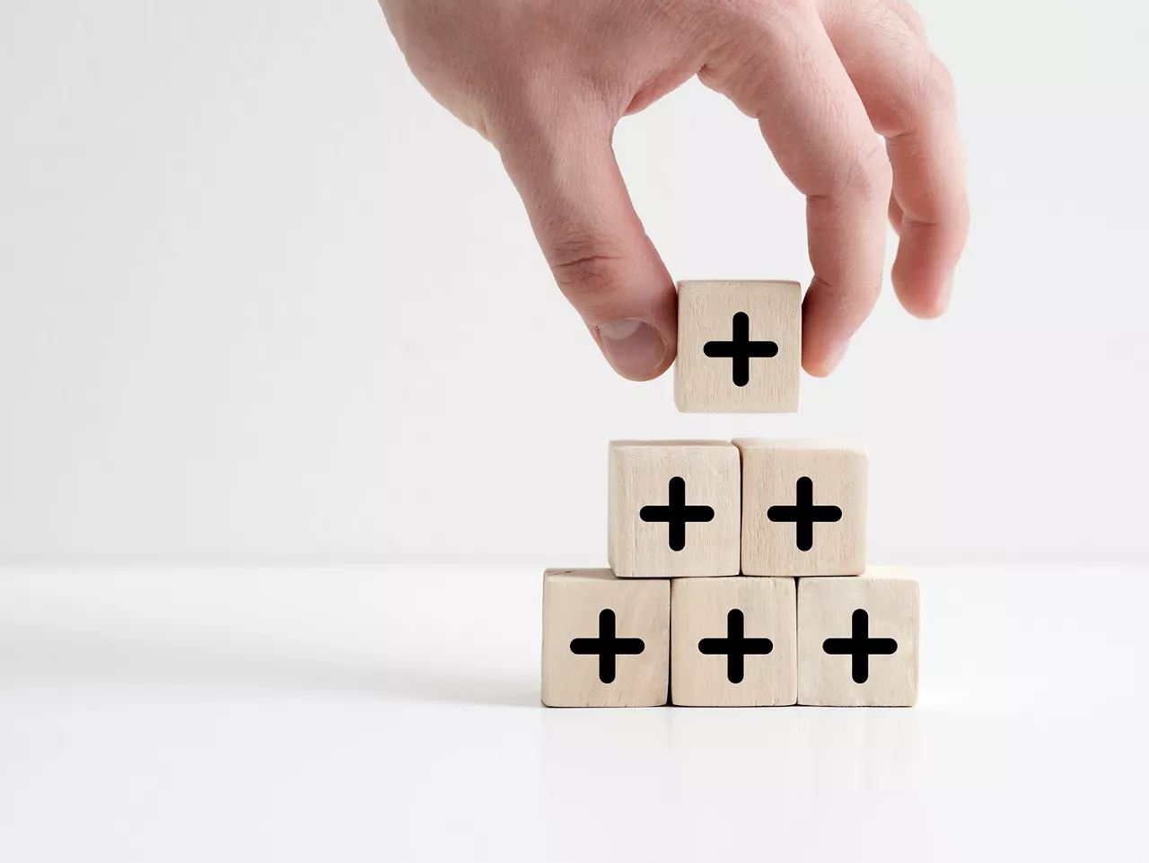 Added value or increasing benefits concept. Progress and profit to benefit growth and development in business. Hand places cube with plus symbol on top of the wooden cube pyramid.