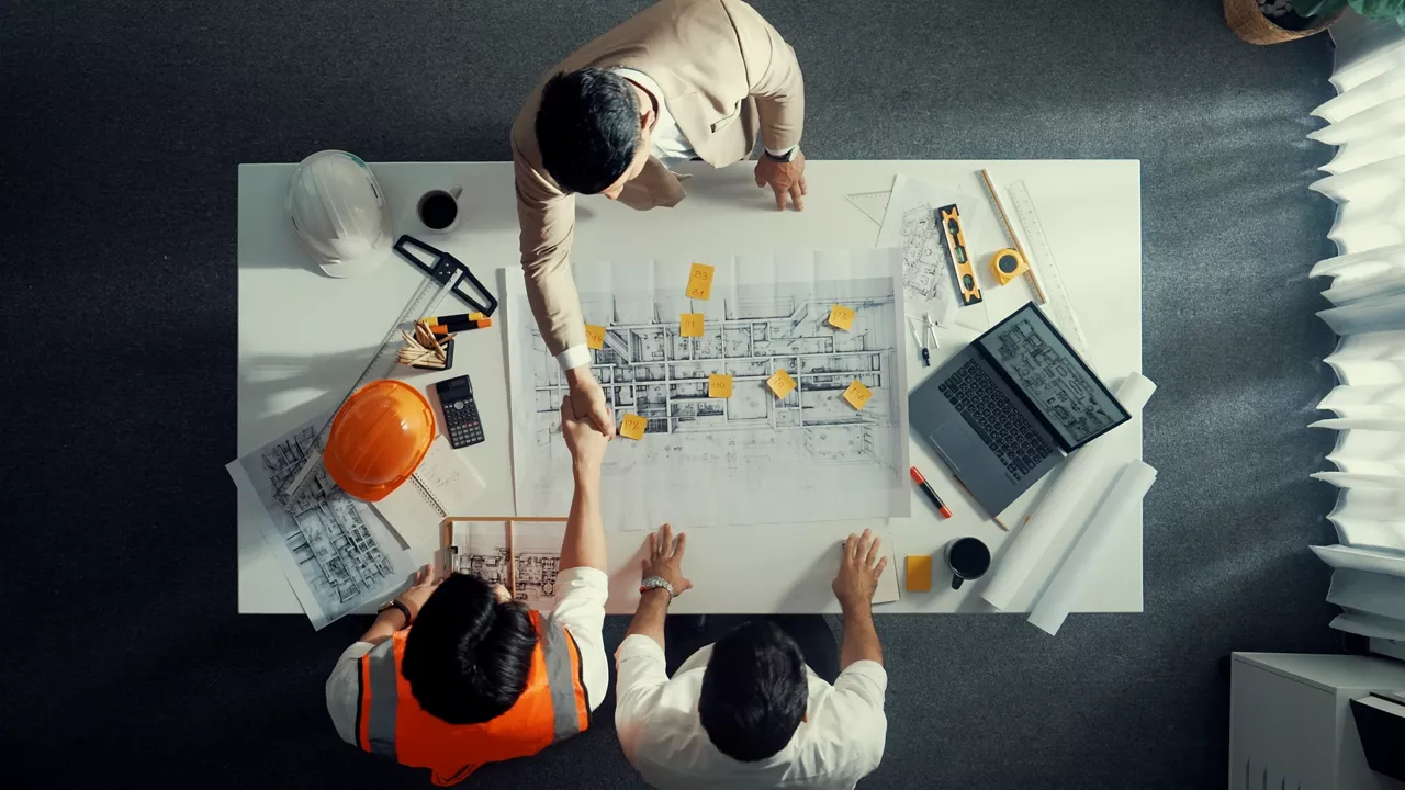 Top down aerial view of architect engineer team shake hands and discussing about building construction. Group of diverse people working together to plan and design by using blueprint. Alimentation.