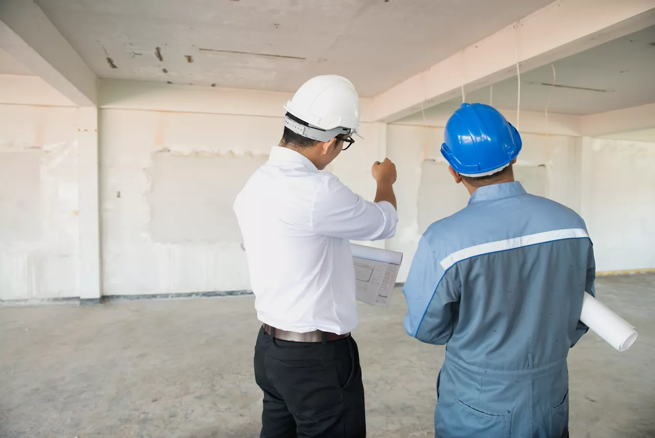 Back view of male engineer and worker checking indoor building construction site.