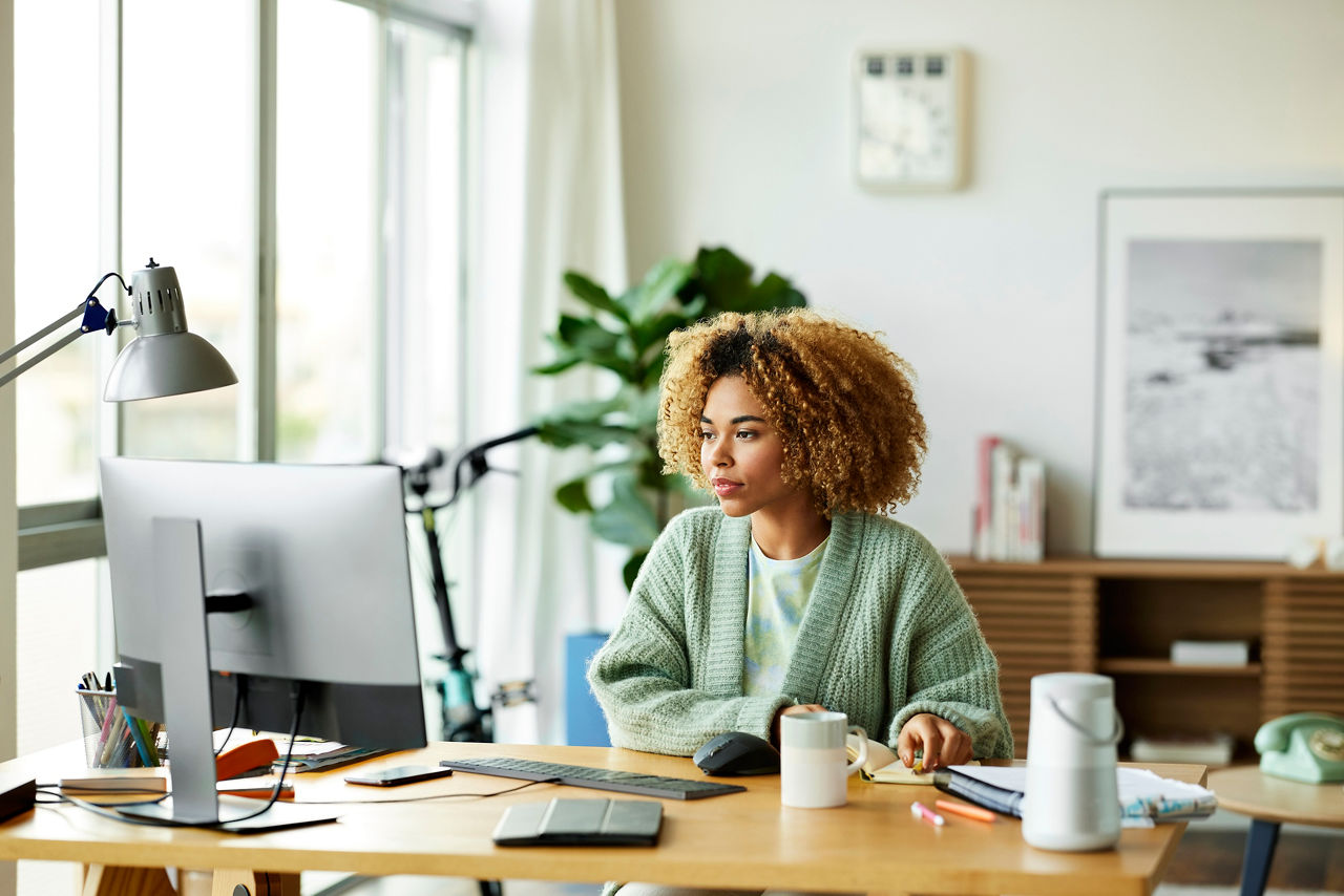 Businesswoman using computer at desk. Female professional is working at home office. She is looking at desktop PC.