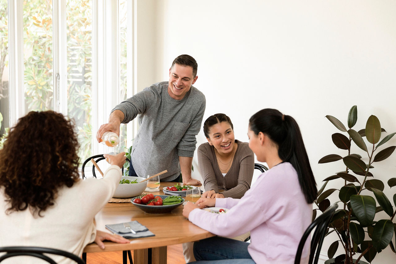 Family at breakfast table with man pouring juice into glass