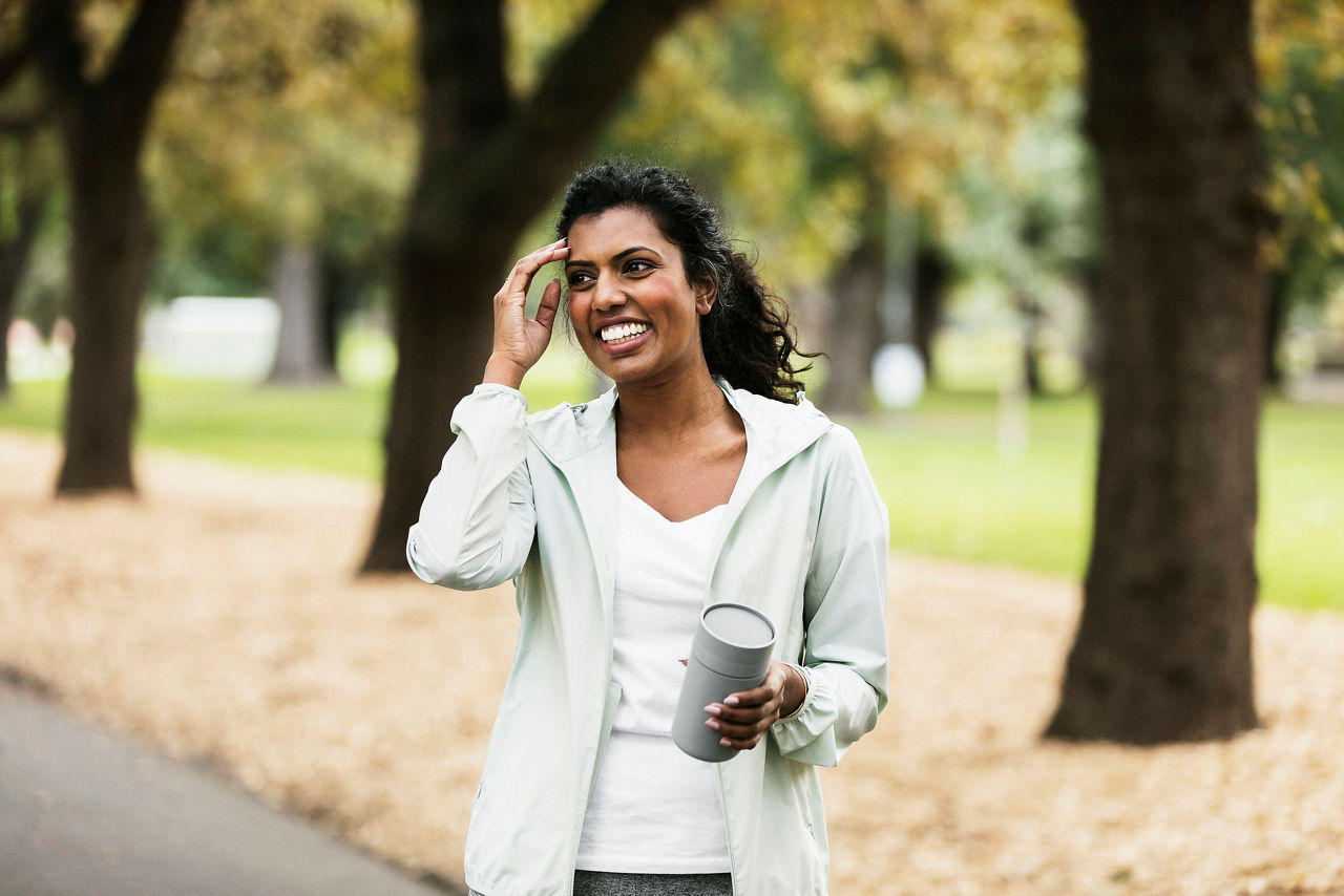 Woman walking in the park with takeaway coffee cup in hand
