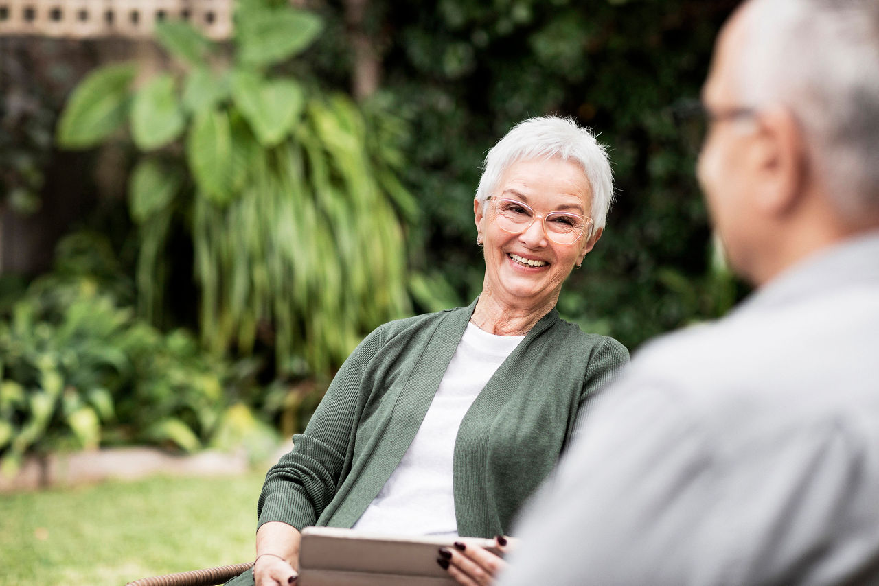 Senior woman holding tablet talking to man in the garden