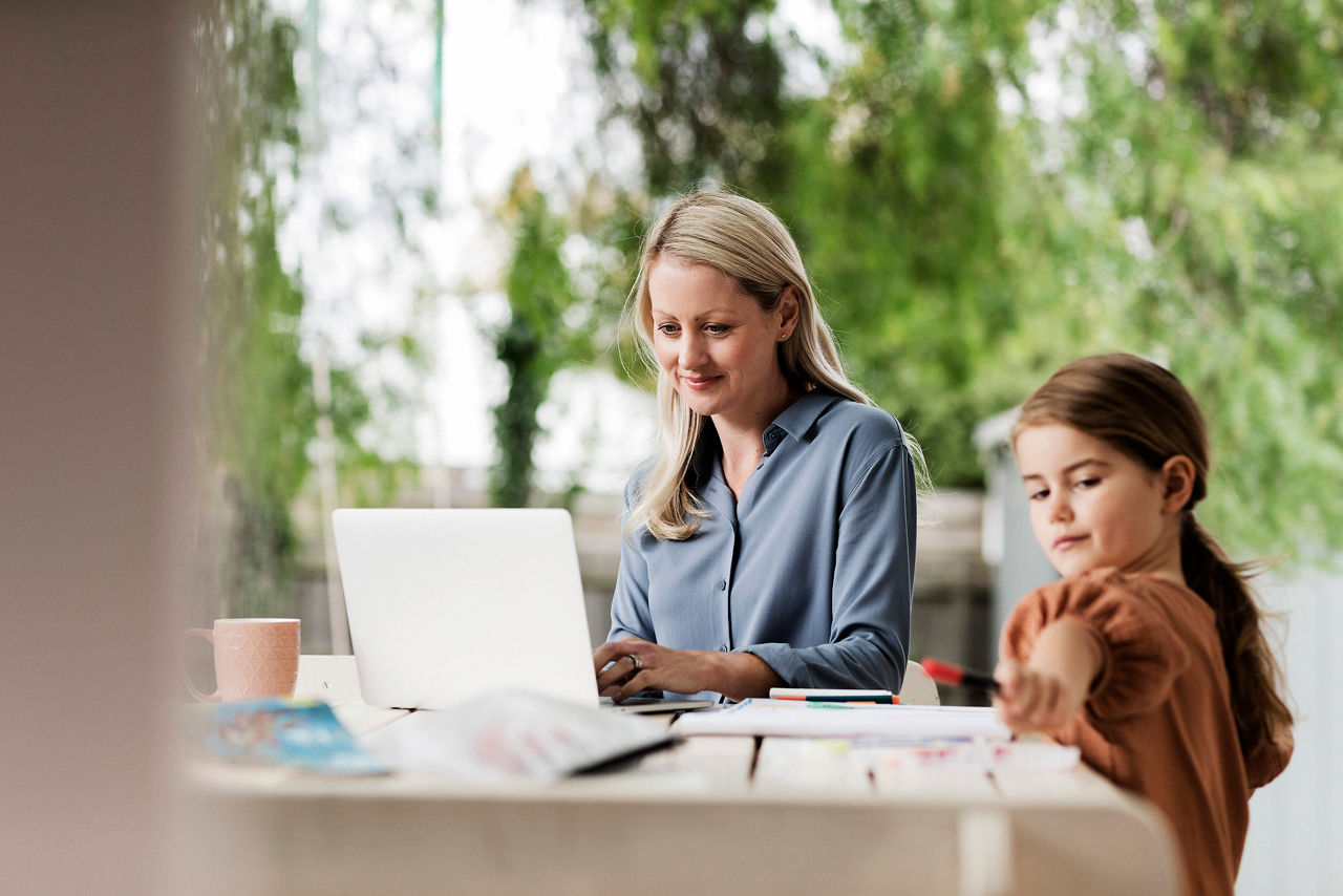 Woman with laptop and child with paper and pens at outdoor tabl