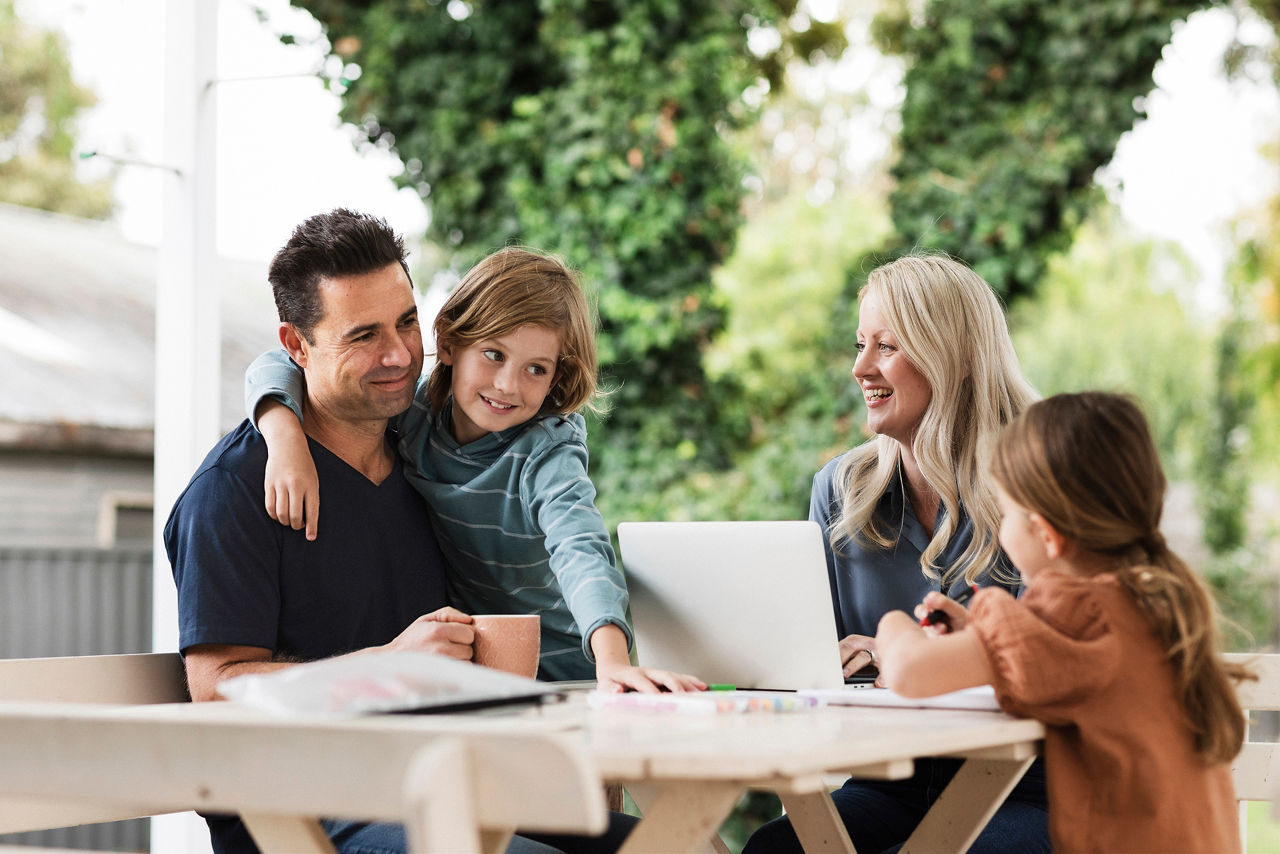 Young family at outdoors table with laptop, tea and crayons