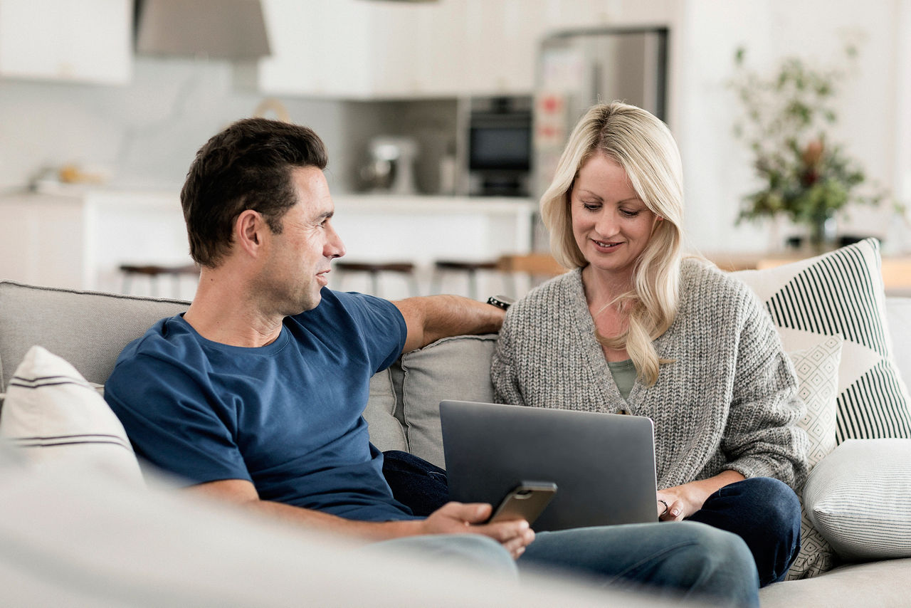 Couple talking on the sofa, man holding mobile phone, woman looking at laptop