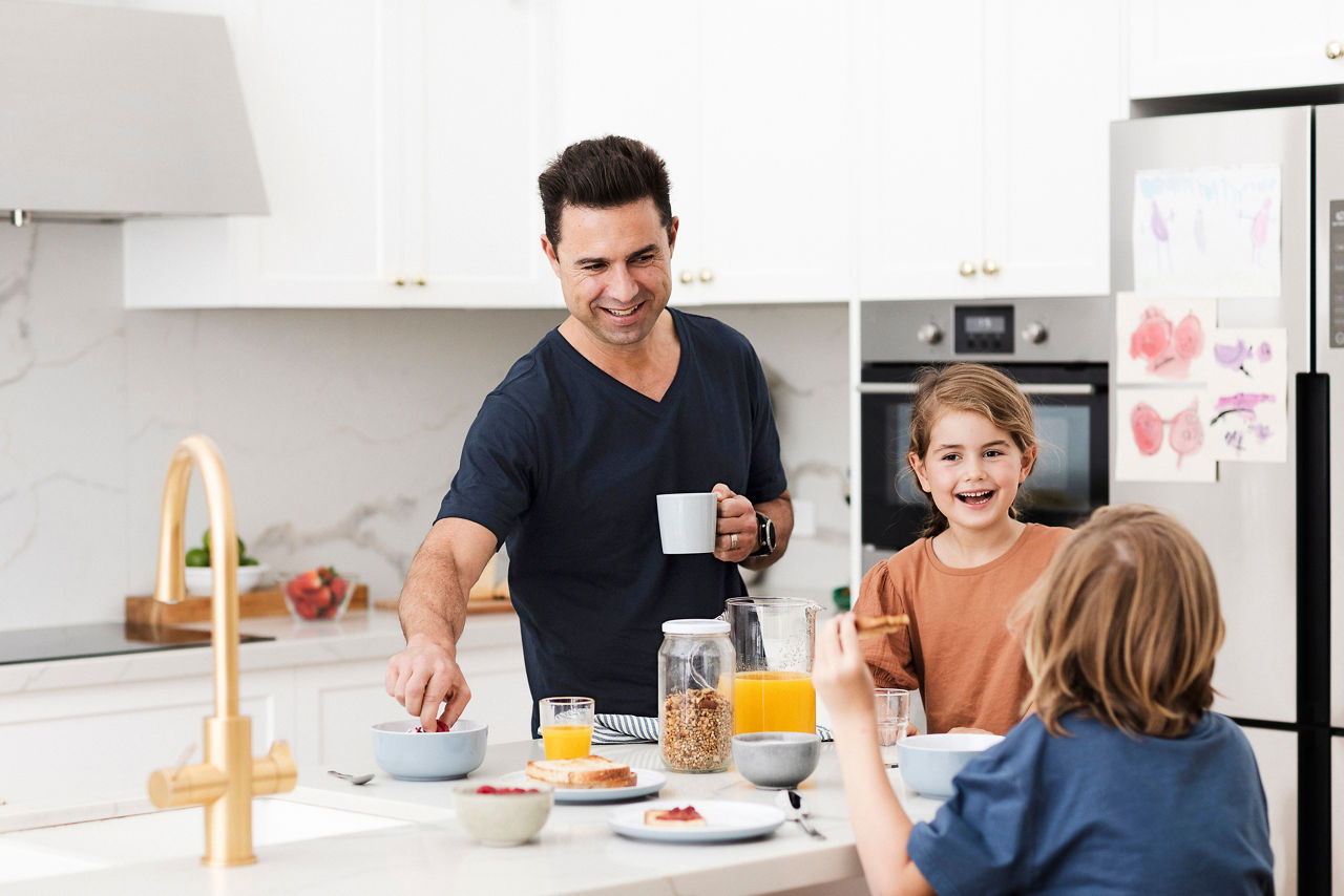 Father with two young children at the kitchen bench eating breakfast