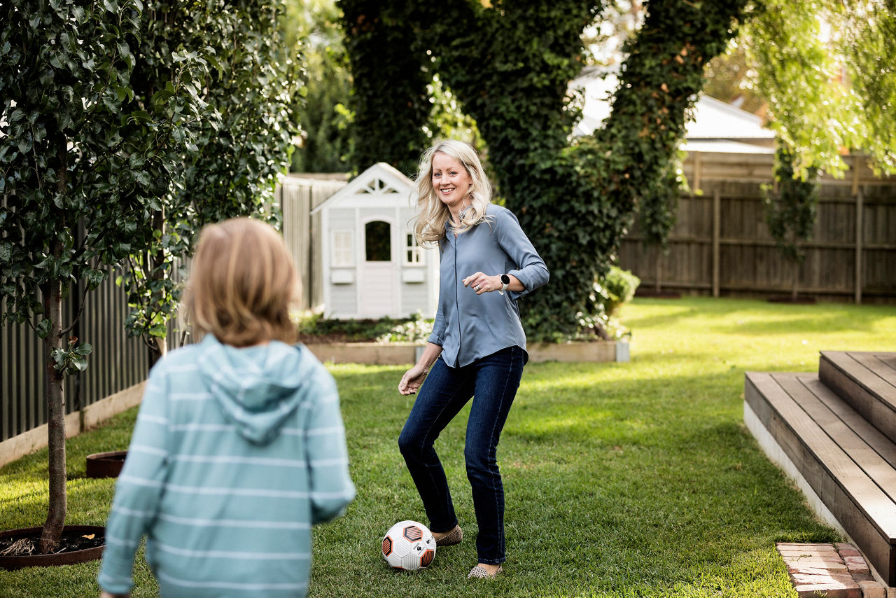 Mother kicking soccer ball with child in the backyard
