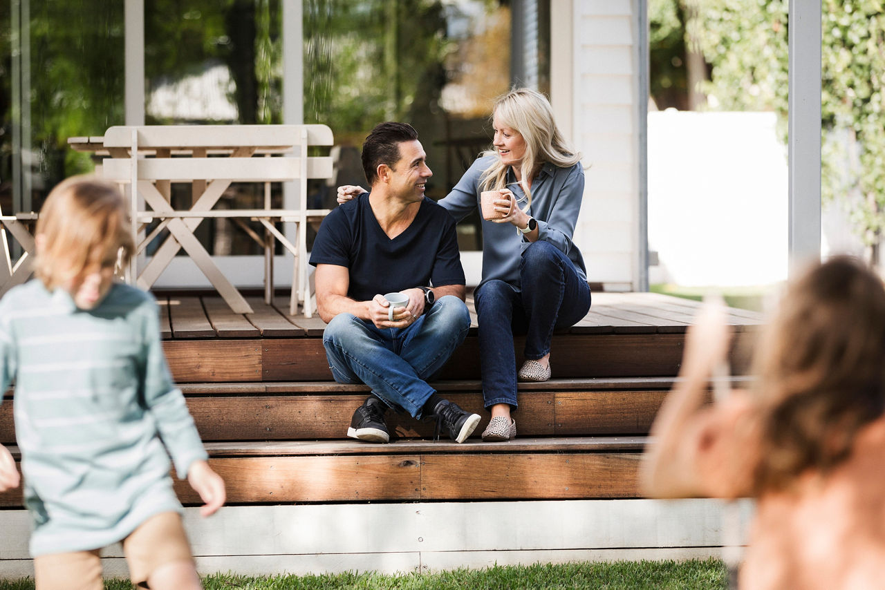 Young family in the backyard, children playing with parents drinking tea on the patio