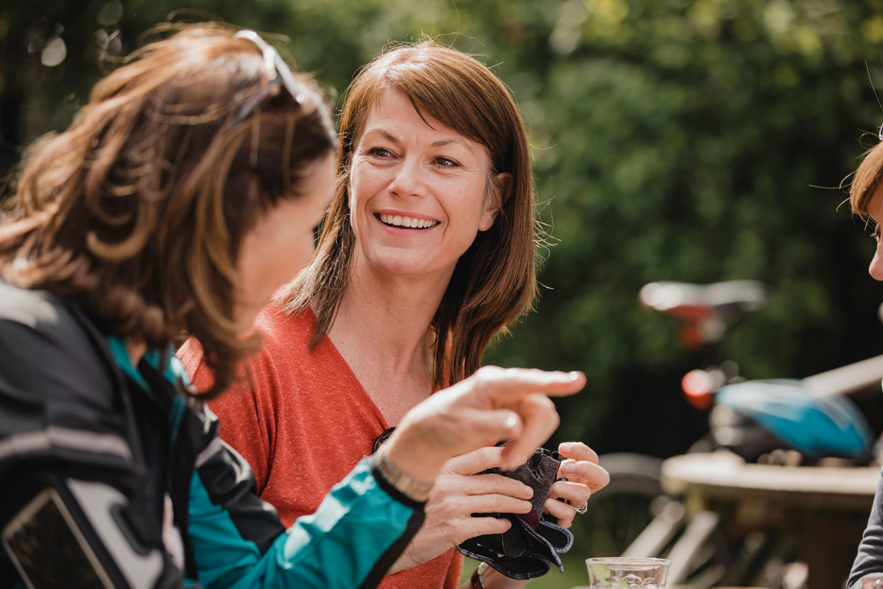 Small group of mature female cyclists sitting down in the outside seating area of a cafe. Tey are enjoying some refreshments as they take a break.