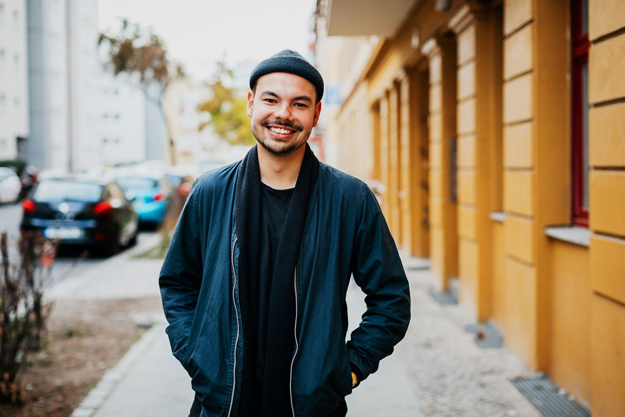 A portrait of a stylish young man standing in a city street, smiling.