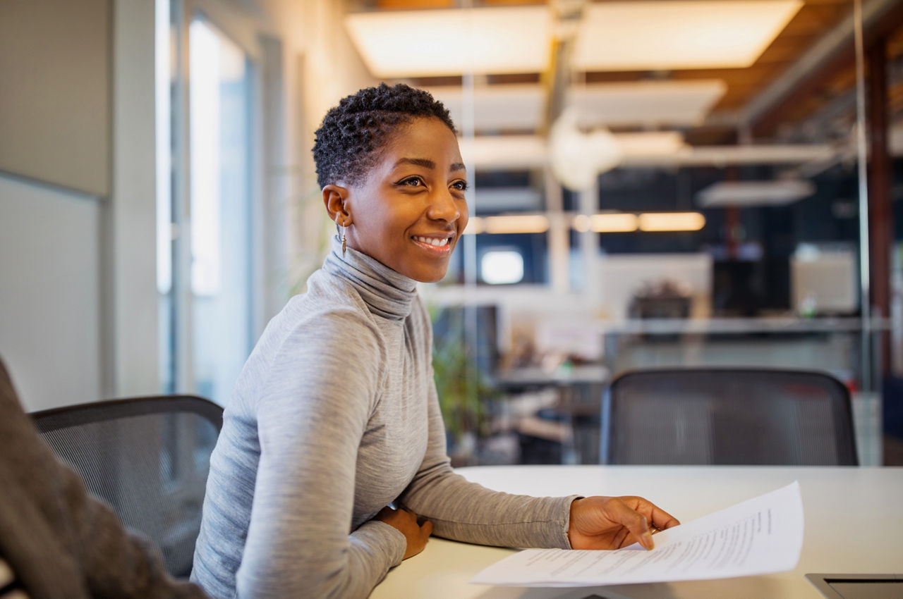 Mid adult woman sitting at table with a document in office. Businesswoman in casuals working in office.