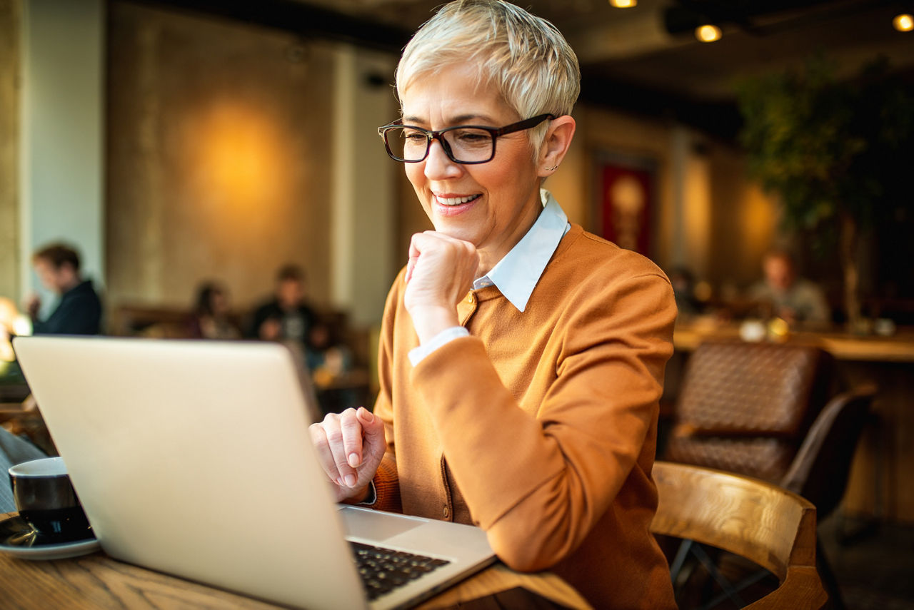 Smiling business woman working from the bar. She is using laptop while having a coffee