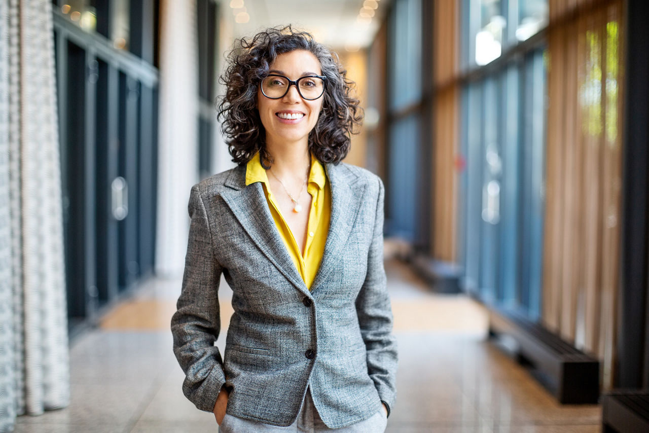 Happy mature businesswoman standing with her hands in pocket outside an auditorium. Smiling female entrepreneur outside convention center.