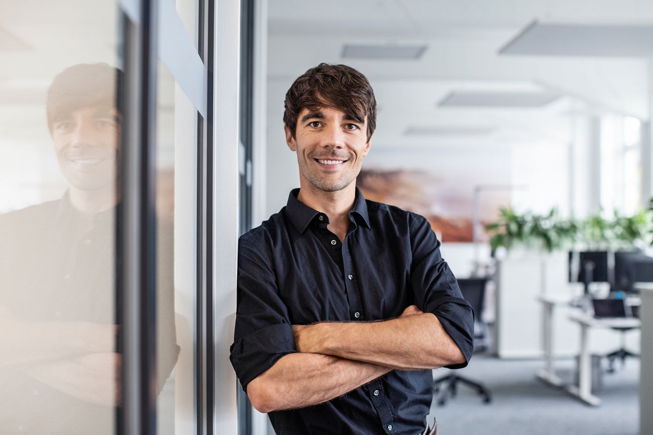 Portrait of confident businessman with arms crossed leaning on wall in creative office