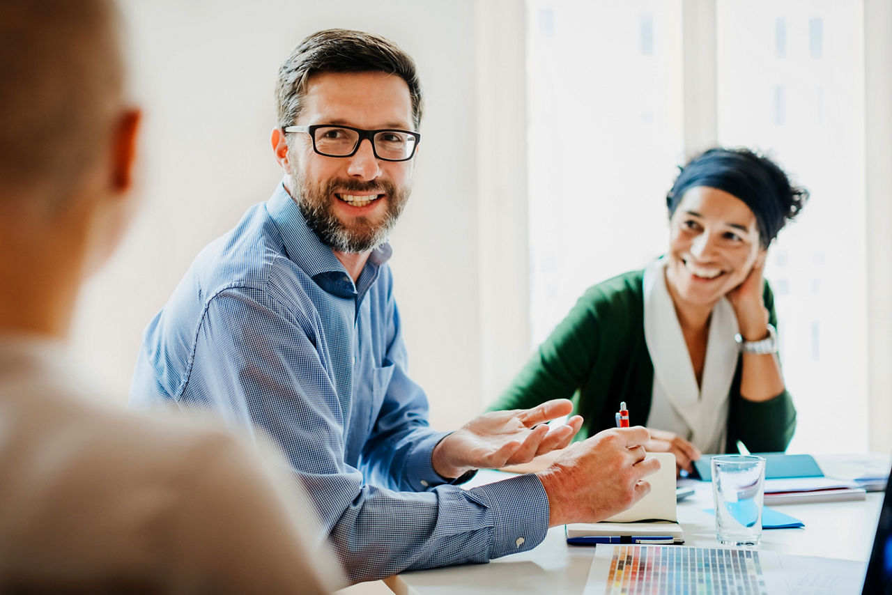 A manager sitting at a desk and talking with his employees  during a meeting at the office.