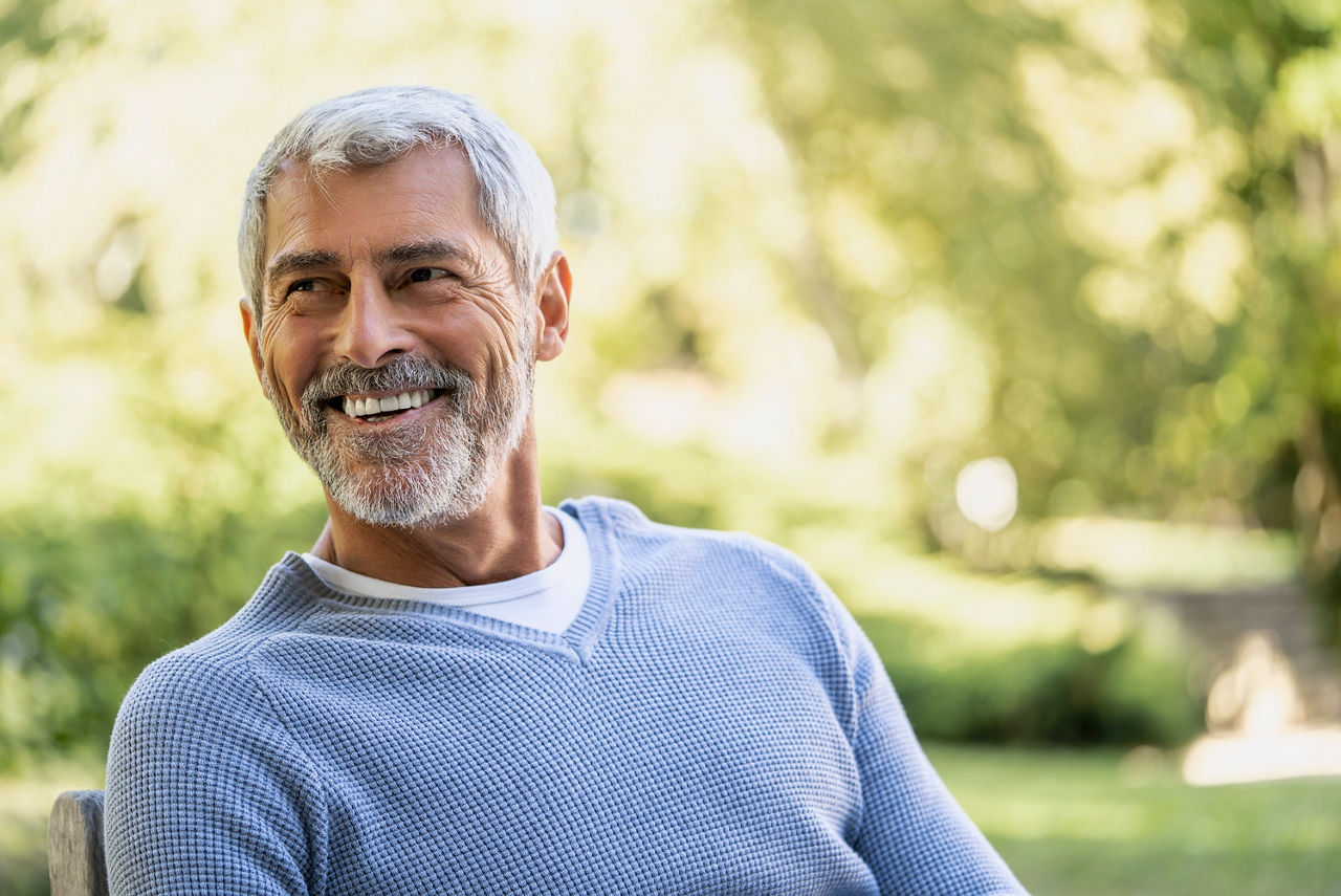 Smiling mature man looking away while sitting on chair in backyard