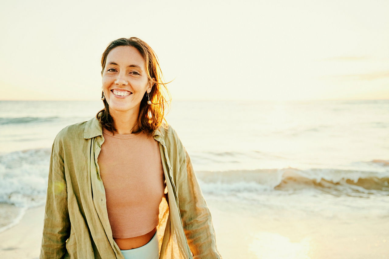 Medium wide shot portrait of smiling woman on tropical beach at sunrise