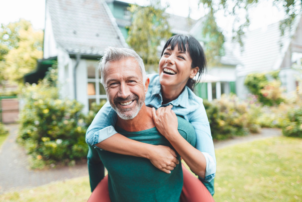 Happy man giving piggyback ride to woman in backyard