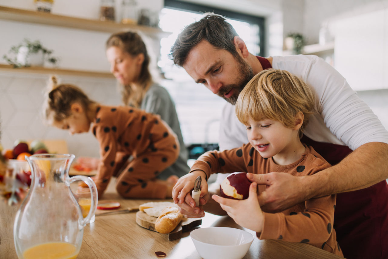 Cheerful parents with small children preparing food at home together.