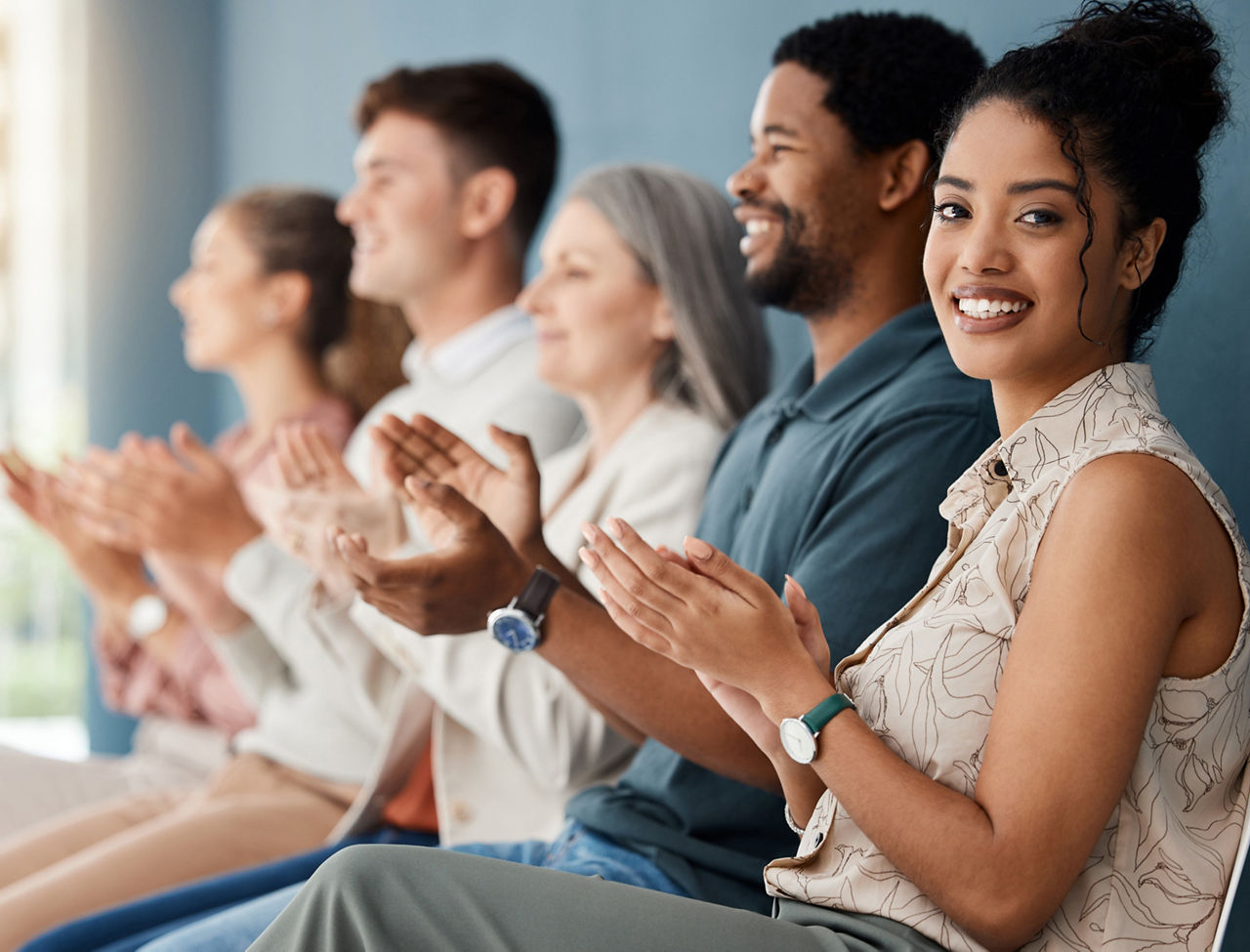 Group of cheerful businesspeople clapping while sitting in a row in a meeting together. Portrait of a young mixed race businesswoman clapping while sitting with colleagues in an office at work
