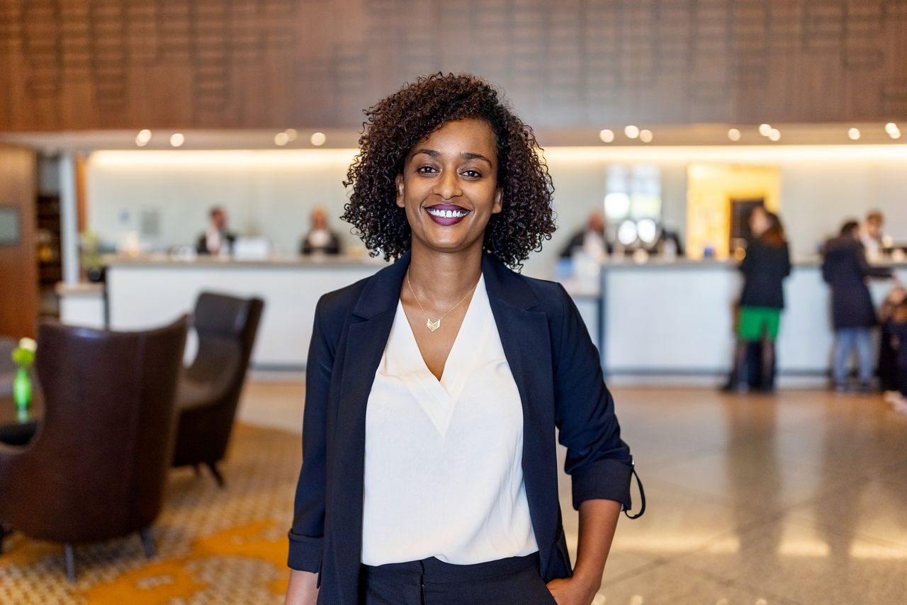 Portrait to African businesswoman at hotel lobby. Female with curly hair in businesswear on business trip looking at camera and smiling at hotel lounge.