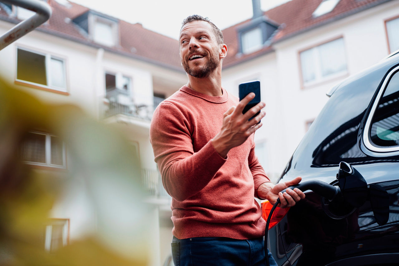 Happy man with smart phone charging electric car at station