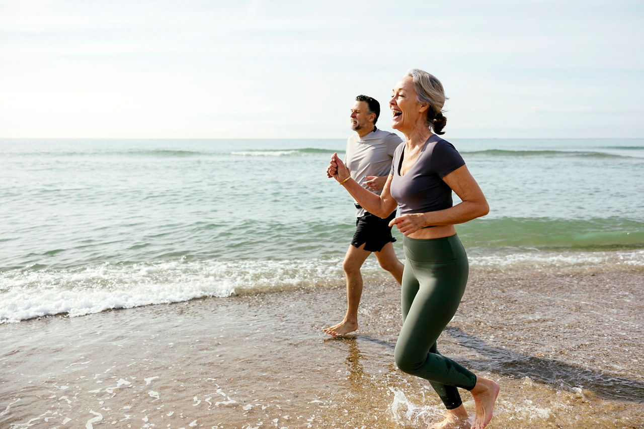 Happy mature couple laughing and running in water at beach