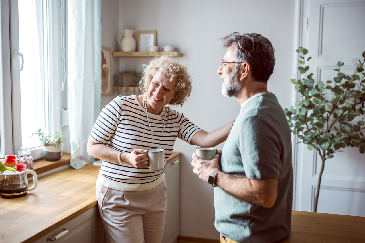 Mature couple standing in front of kitchen window and drinking tea or coffee. Enjoying in morning.