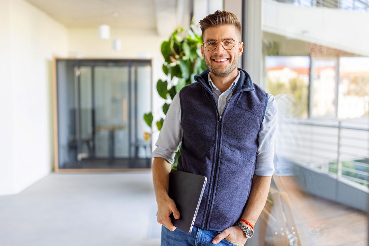 Portrait of a happy young man standing at startup office. Confident businessman at startup office looking at camera and smiling.