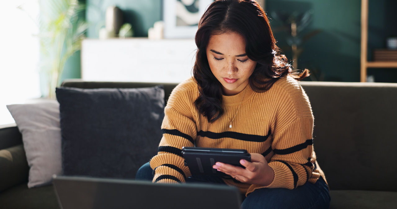 Tablet, freelancer and woman in home with laptop for editing, review or journalist check story. Digital technology, serious and remote work with app for report, news and research article on internet