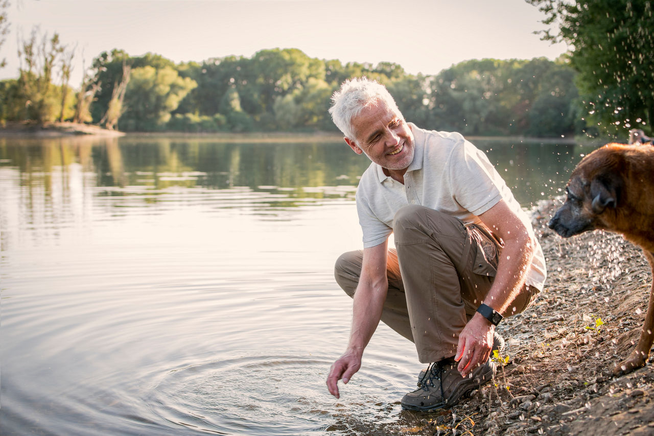 Senior, Mann spielt mit seinem Hund am See, NRW, Deutschland
