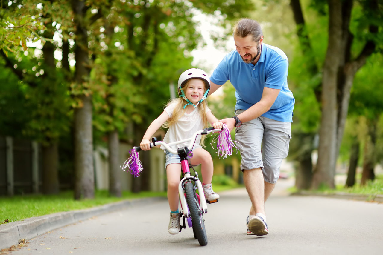 Happy father teaching his little daughter to ride a bicycle. Child learning to ride a bike. Family activities at summer.