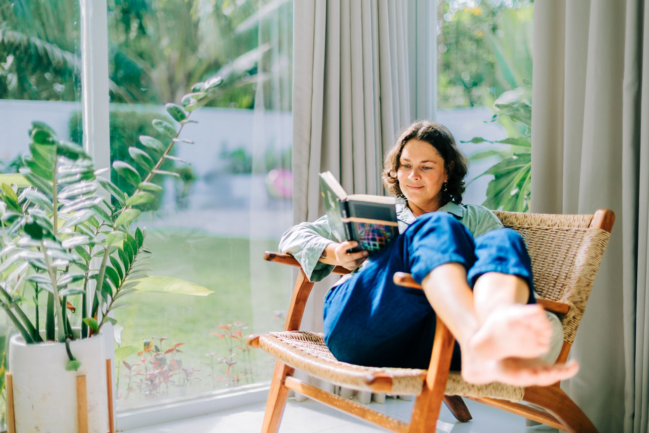Woman enjoying reading book in armchair by window