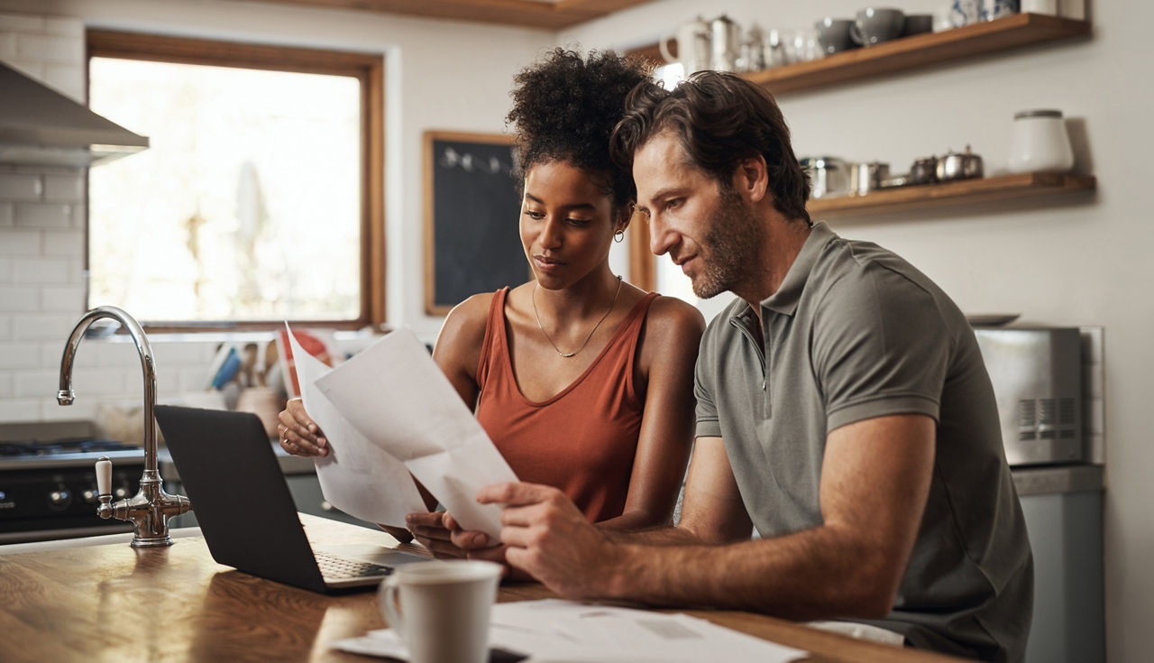 Cropped shot of a couple using their laptop and going through paperwork at home