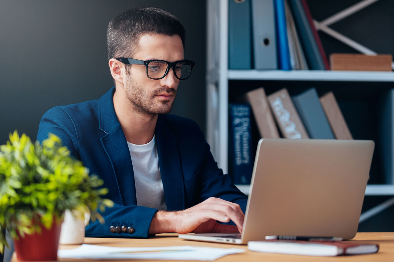 Concentrated young man working on laptop while sitting at his working place in office